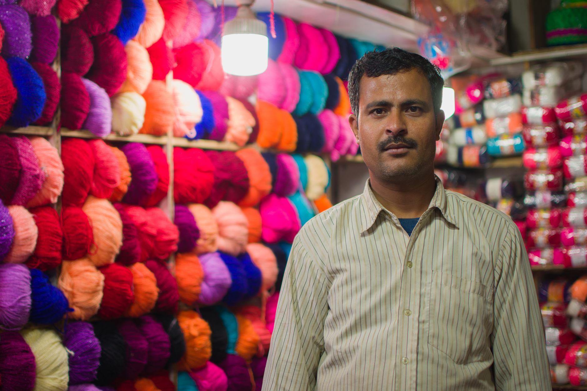 Shopkeeper standing beside colorful textile rolls
